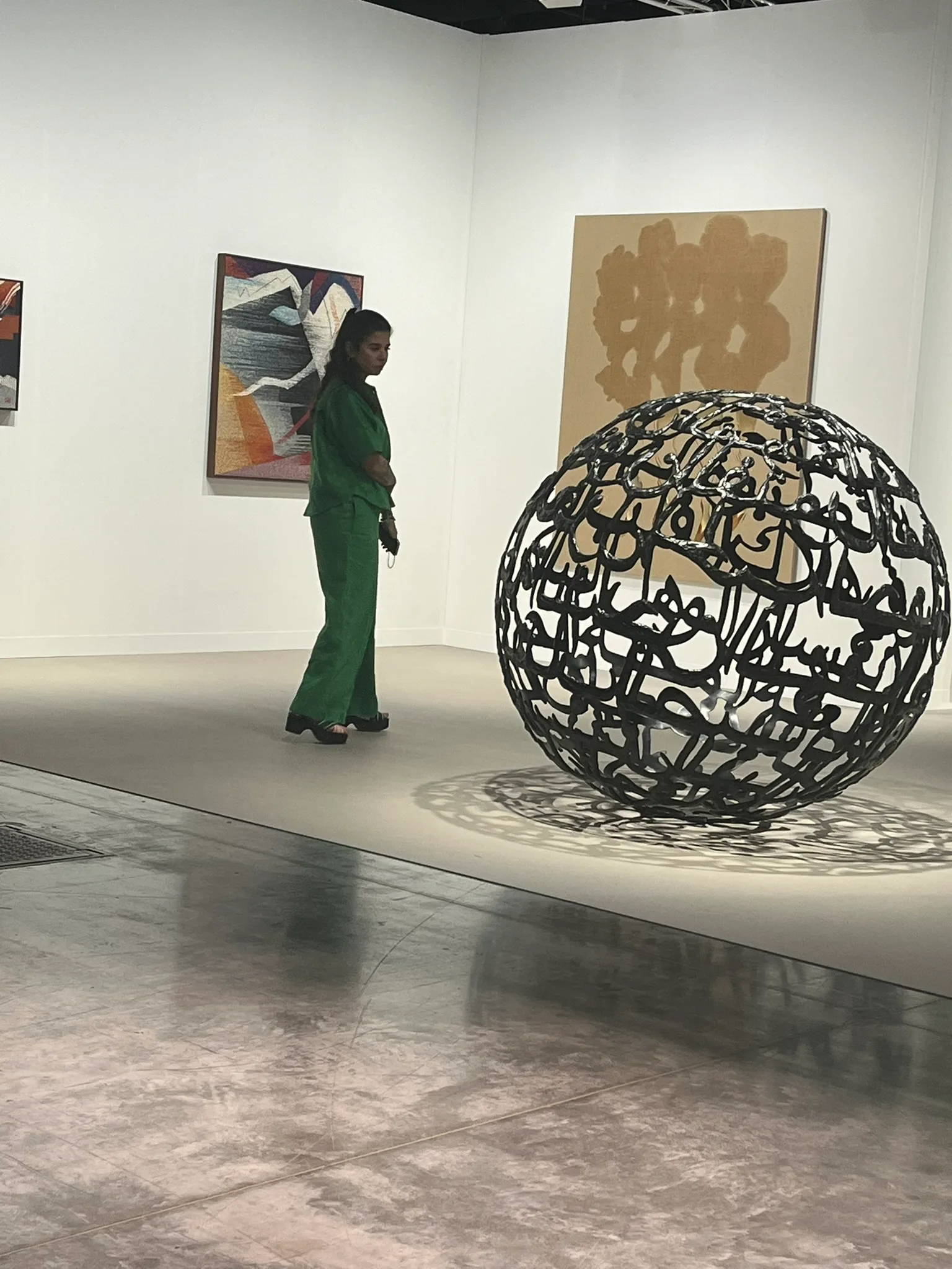 Wided Khadraoui at a contemporary art fair, standing before a spherical calligraphy sculpture
