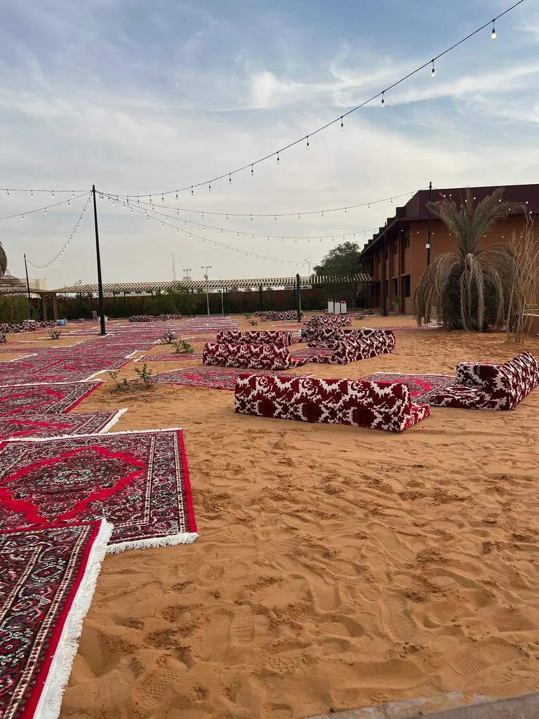An outdoor majlis of patterned rugs and cushions set on desert sand under string lights