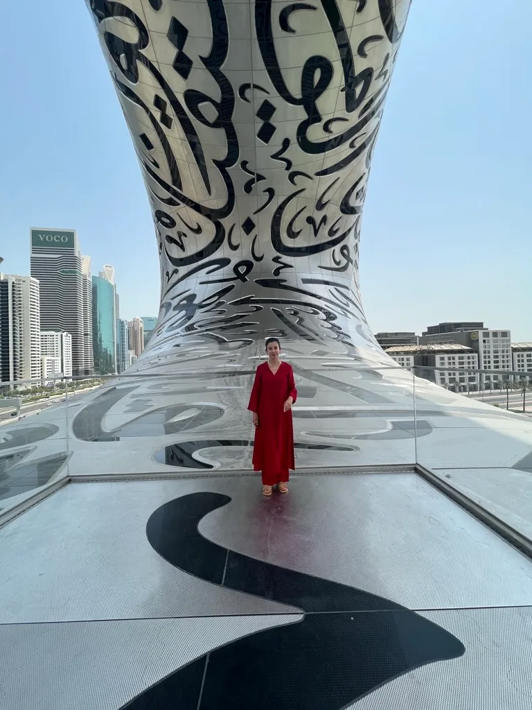 Wided Khadraoui in red standing before the calligraphy facade of the Museum of the Future, Dubai