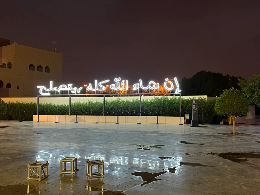 An Arabic neon text installation in a public square at night