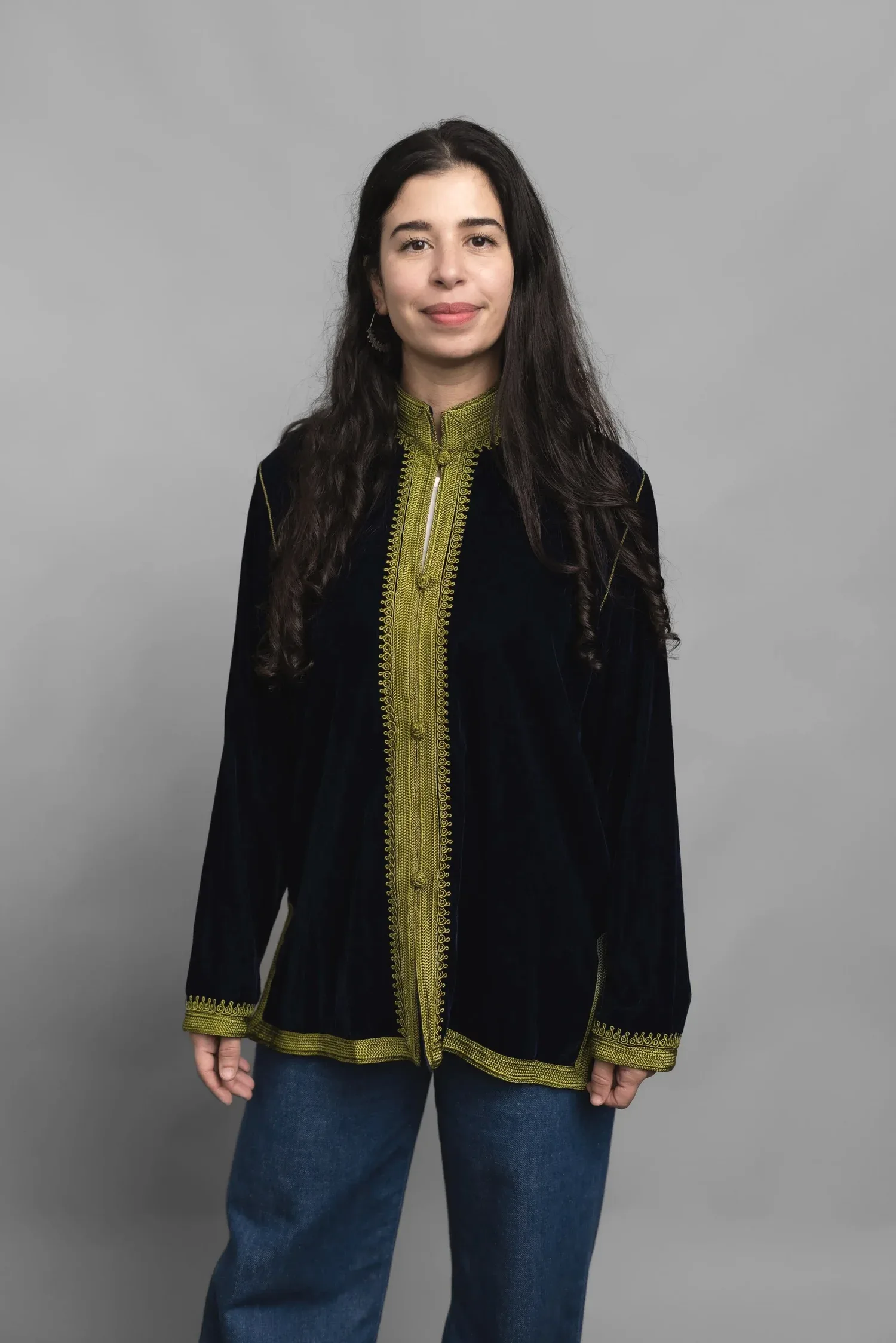 Studio portrait of Dr. Wided Rihana Khadraoui wearing a night-blue velvet jacket with olive embroidery, photographed against a grey background.